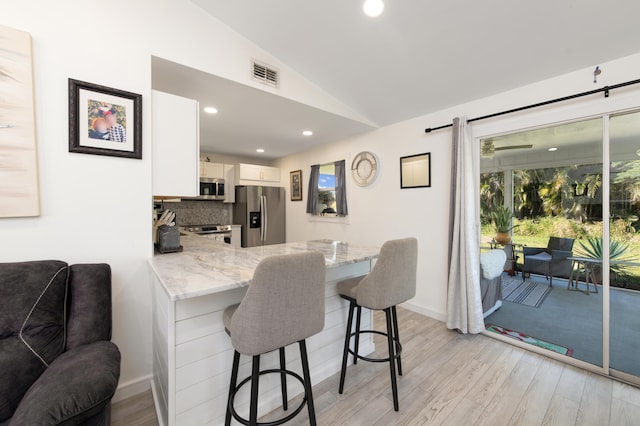 kitchen with appliances with stainless steel finishes, a kitchen breakfast bar, light stone counters, white cabinets, and lofted ceiling