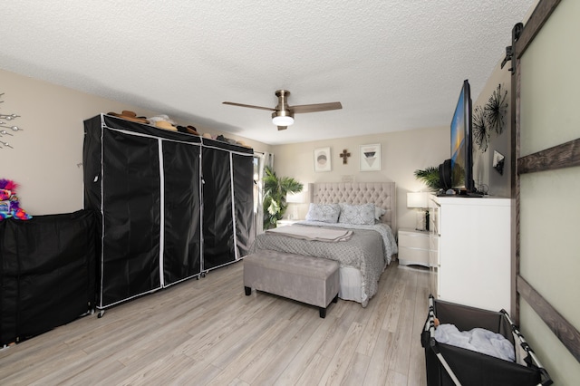 bedroom with light wood-type flooring, a textured ceiling, a barn door, and ceiling fan