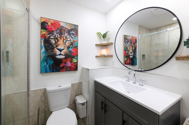 bathroom with walk in shower, vanity, tile walls, and toilet