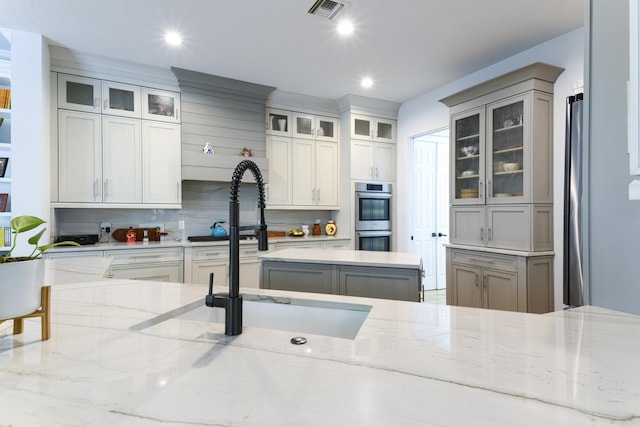 kitchen featuring gray cabinets, light stone counters, stainless steel double oven, and sink