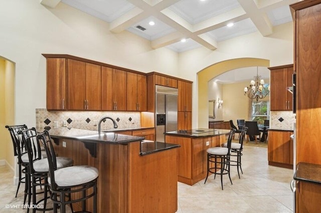 kitchen featuring built in fridge, a notable chandelier, an island with sink, decorative light fixtures, and a kitchen bar