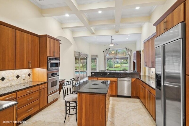 kitchen featuring appliances with stainless steel finishes, a breakfast bar, ceiling fan, beamed ceiling, and a kitchen island