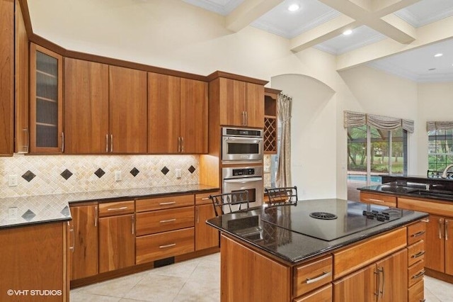 kitchen with decorative backsplash, black electric stovetop, stainless steel double oven, beam ceiling, and a center island