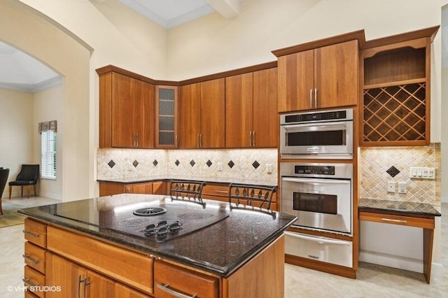 kitchen featuring a high ceiling, black electric stovetop, dark stone countertops, a kitchen island, and stainless steel double oven