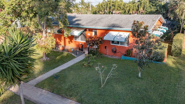 ranch-style home with roof with shingles, a front yard, and stucco siding