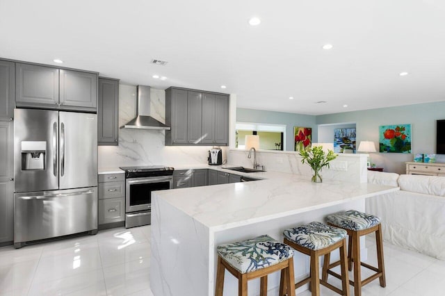 kitchen featuring wall chimney range hood, sink, appliances with stainless steel finishes, kitchen peninsula, and a breakfast bar area