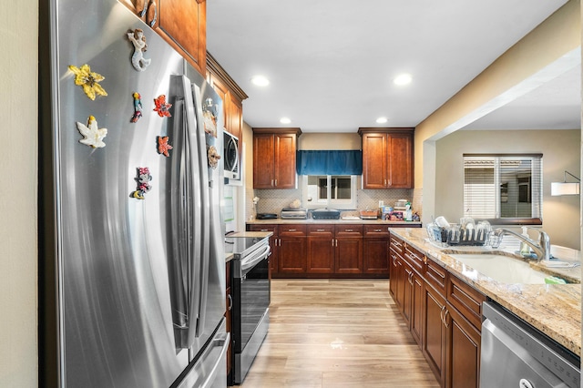 kitchen featuring backsplash, sink, light stone countertops, light hardwood / wood-style floors, and stainless steel appliances