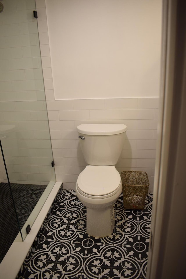 bathroom featuring tile patterned flooring, tile walls, toilet, and tiled shower