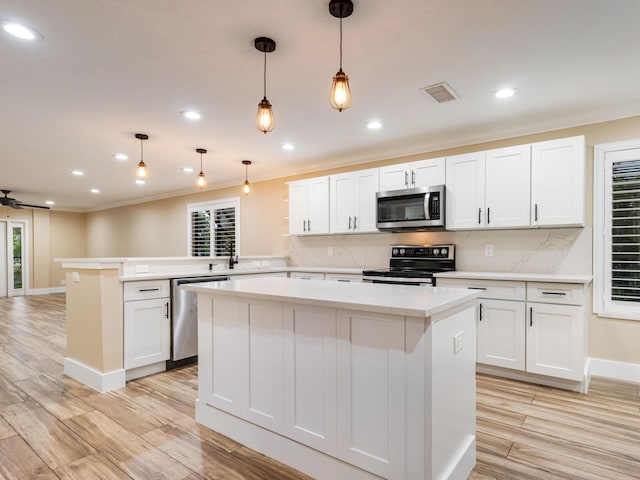 kitchen featuring appliances with stainless steel finishes, white cabinetry, hanging light fixtures, tasteful backsplash, and kitchen peninsula