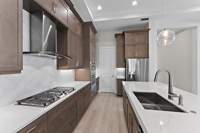 kitchen featuring sink, appliances with stainless steel finishes, hanging light fixtures, light stone counters, and wall chimney exhaust hood