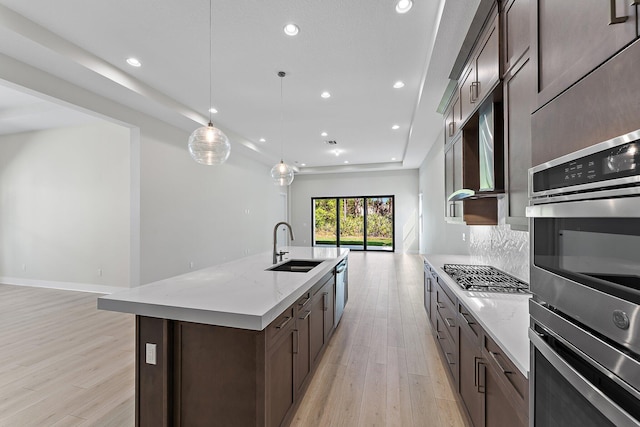 kitchen featuring sink, hanging light fixtures, light stone counters, stainless steel appliances, and a center island with sink