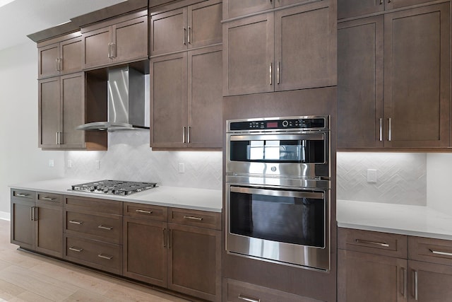 kitchen featuring stainless steel appliances, light stone countertops, wall chimney range hood, and backsplash