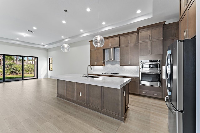 kitchen with appliances with stainless steel finishes, sink, hanging light fixtures, a tray ceiling, and wall chimney range hood