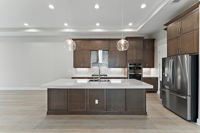 kitchen featuring decorative light fixtures, dark brown cabinets, an island with sink, stainless steel appliances, and wall chimney range hood