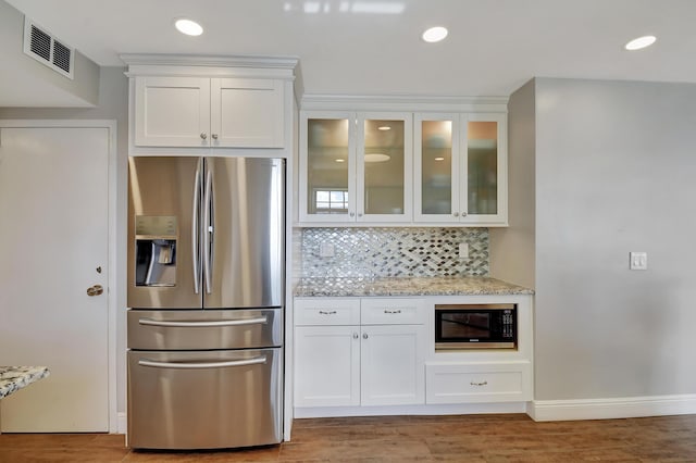 kitchen with black microwave, light stone countertops, white cabinets, stainless steel fridge with ice dispenser, and decorative backsplash