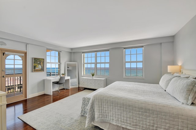 bedroom with access to exterior, dark wood-type flooring, and a water view