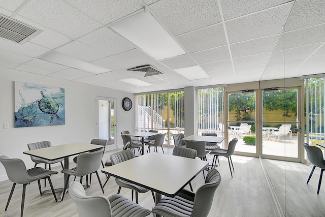 dining room with expansive windows, light hardwood / wood-style flooring, and a drop ceiling