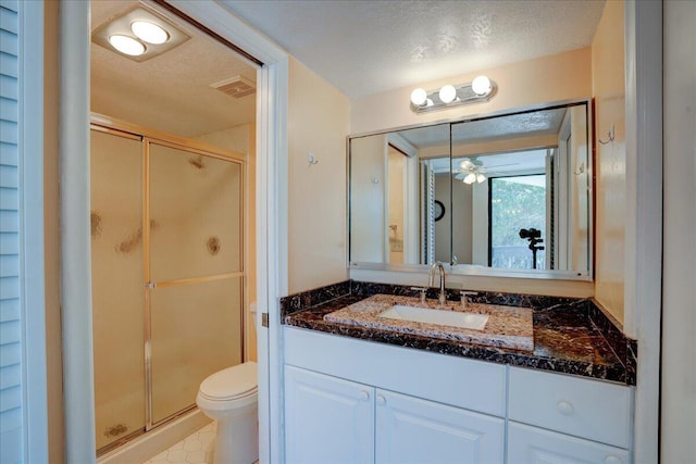 bathroom with ceiling fan, a textured ceiling, toilet, a shower with door, and vanity