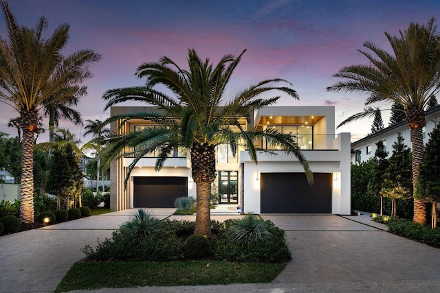 contemporary house with decorative driveway, a balcony, an attached garage, and stucco siding