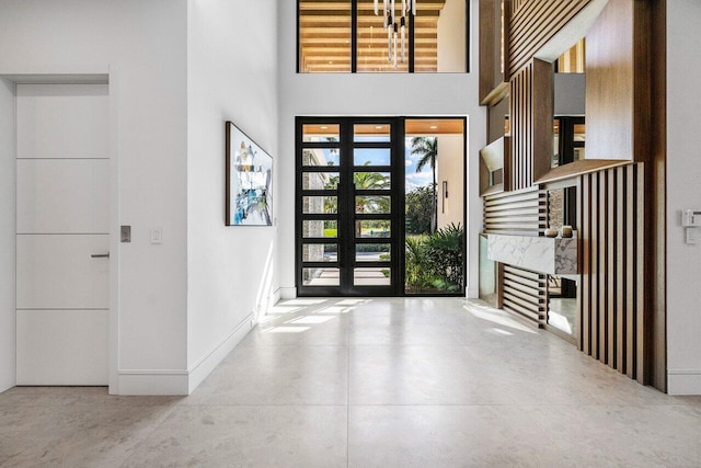 foyer featuring concrete flooring, a towering ceiling, and baseboards