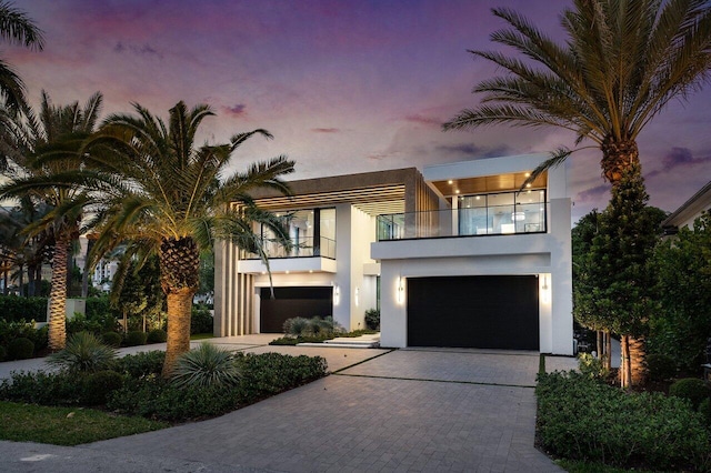 contemporary home with decorative driveway, a balcony, an attached garage, and stucco siding