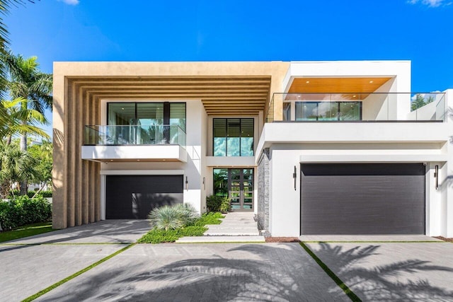 contemporary house with a garage, a balcony, driveway, and stucco siding