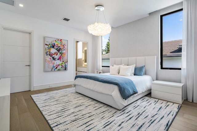 bedroom featuring visible vents, a notable chandelier, ensuite bath, and wood finished floors