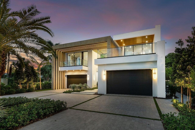 modern home with decorative driveway, a balcony, an attached garage, and stucco siding