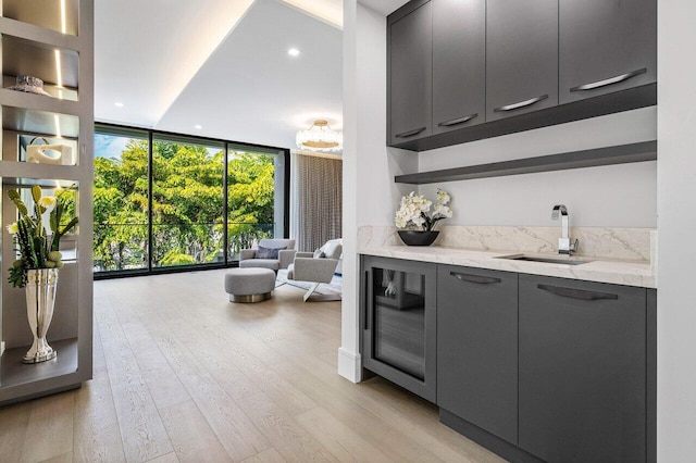 interior space with wine cooler, wet bar, a sink, a wall of windows, and light wood-type flooring