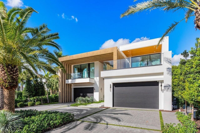 modern home with a garage, decorative driveway, a balcony, and stucco siding