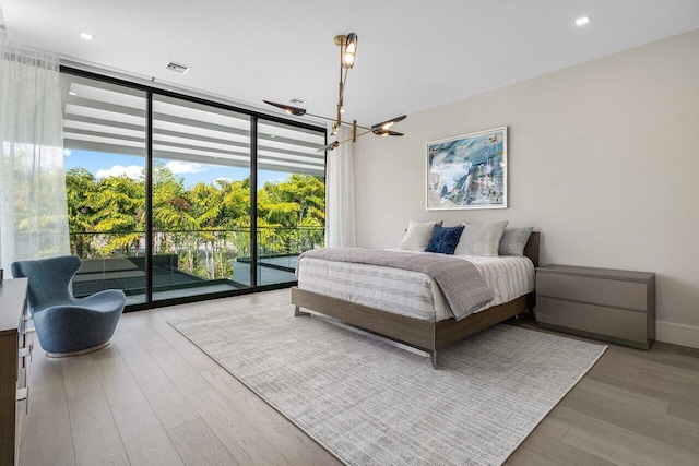 bedroom with wood finished floors, visible vents, access to outside, expansive windows, and an inviting chandelier