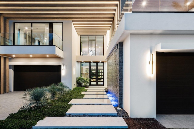 doorway to property featuring a garage, a balcony, and stucco siding