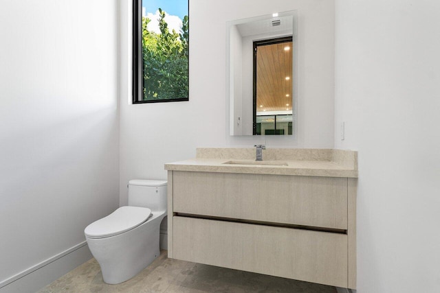 half bathroom with vanity, toilet, and baseboards