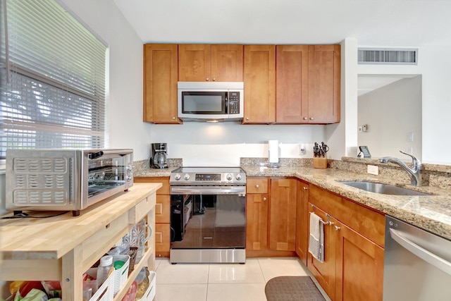 kitchen with sink, light stone countertops, stainless steel appliances, and light tile patterned floors