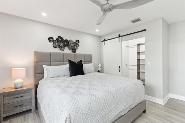 bedroom with a spacious closet, ceiling fan, light hardwood / wood-style floors, and a barn door