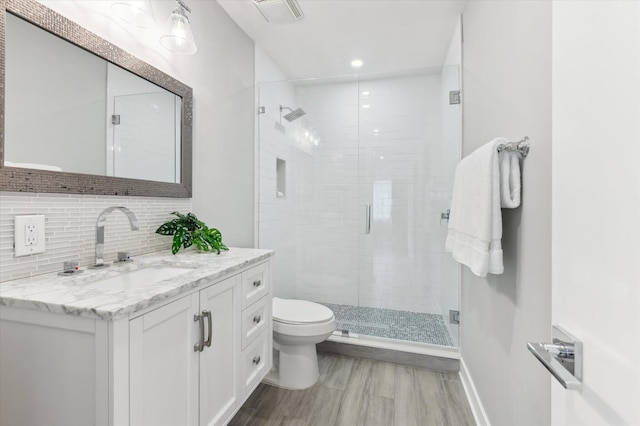 bathroom with tasteful backsplash, vanity, toilet, wood-type flooring, and a shower with shower door