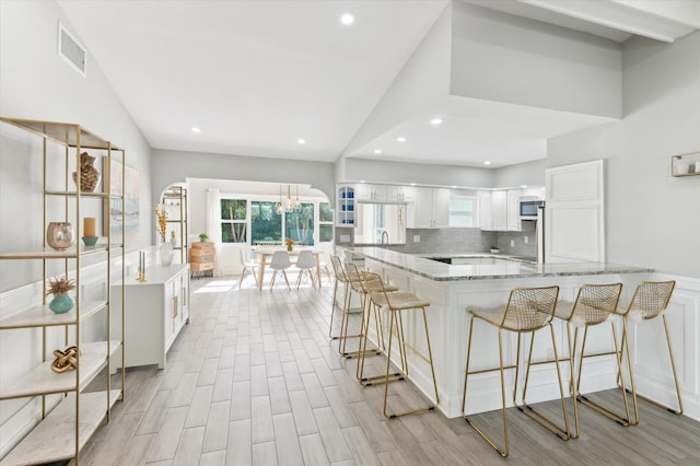 kitchen with white cabinetry, kitchen peninsula, decorative backsplash, light stone countertops, and sink