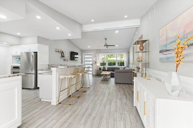 kitchen with a kitchen bar, appliances with stainless steel finishes, light wood-type flooring, vaulted ceiling with beams, and white cabinets