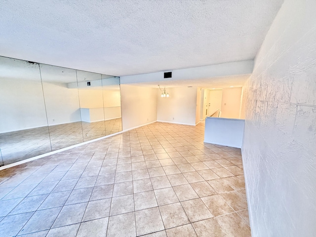 tiled empty room featuring a chandelier and a textured ceiling