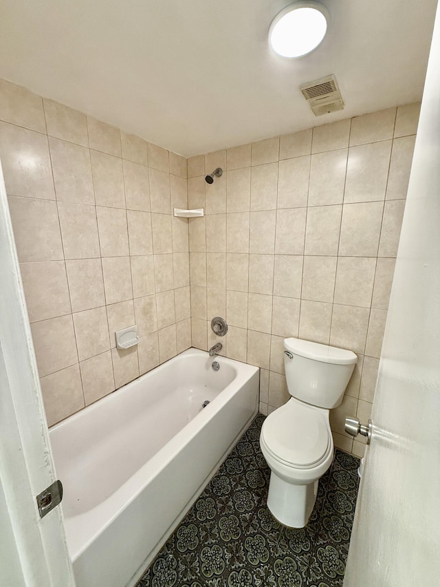 bathroom with toilet, tiled shower / bath, and tile walls