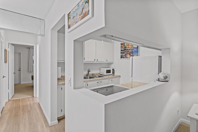 kitchen with white cabinetry, sink, light hardwood / wood-style flooring, kitchen peninsula, and white appliances