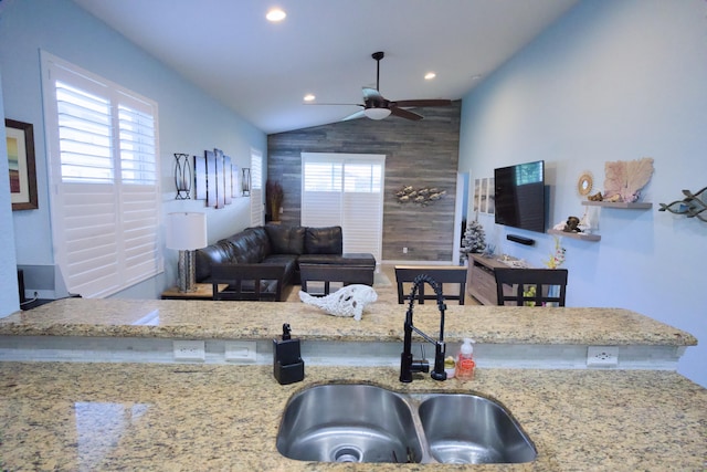 kitchen featuring ceiling fan, light stone countertops, lofted ceiling, and sink