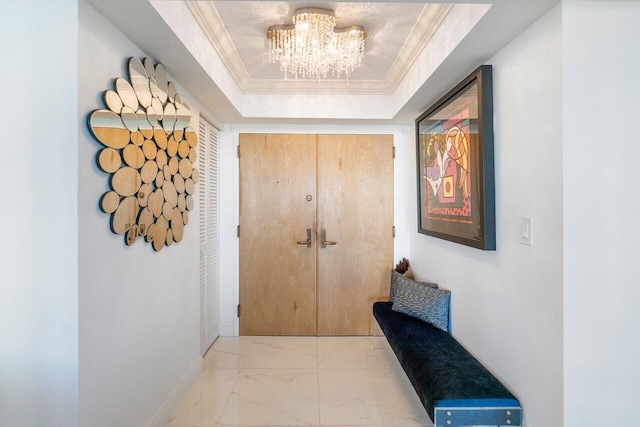 corridor featuring a tray ceiling, crown molding, and an inviting chandelier