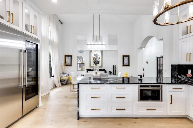 kitchen featuring stainless steel appliances, a notable chandelier, dark stone countertops, white cabinets, and hanging light fixtures