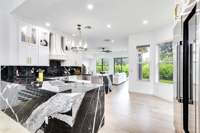 kitchen featuring appliances with stainless steel finishes, premium range hood, dark stone countertops, white cabinetry, and hanging light fixtures