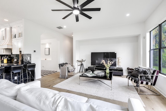 living room with bar, light wood-type flooring, and ceiling fan