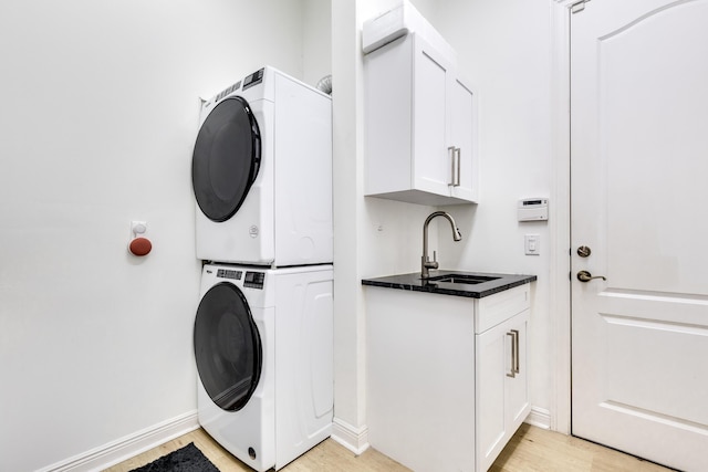 laundry area featuring cabinets, sink, stacked washer / dryer, and light hardwood / wood-style flooring