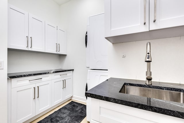 kitchen with stacked washer / dryer, sink, white cabinets, and dark stone counters