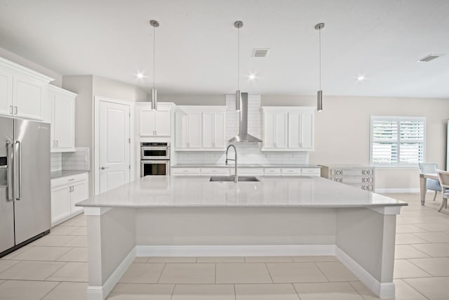 kitchen with pendant lighting, a spacious island, wall chimney range hood, and appliances with stainless steel finishes