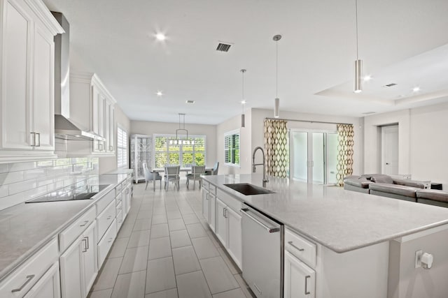 kitchen with white cabinetry, wall chimney range hood, stainless steel dishwasher, a large island with sink, and decorative light fixtures